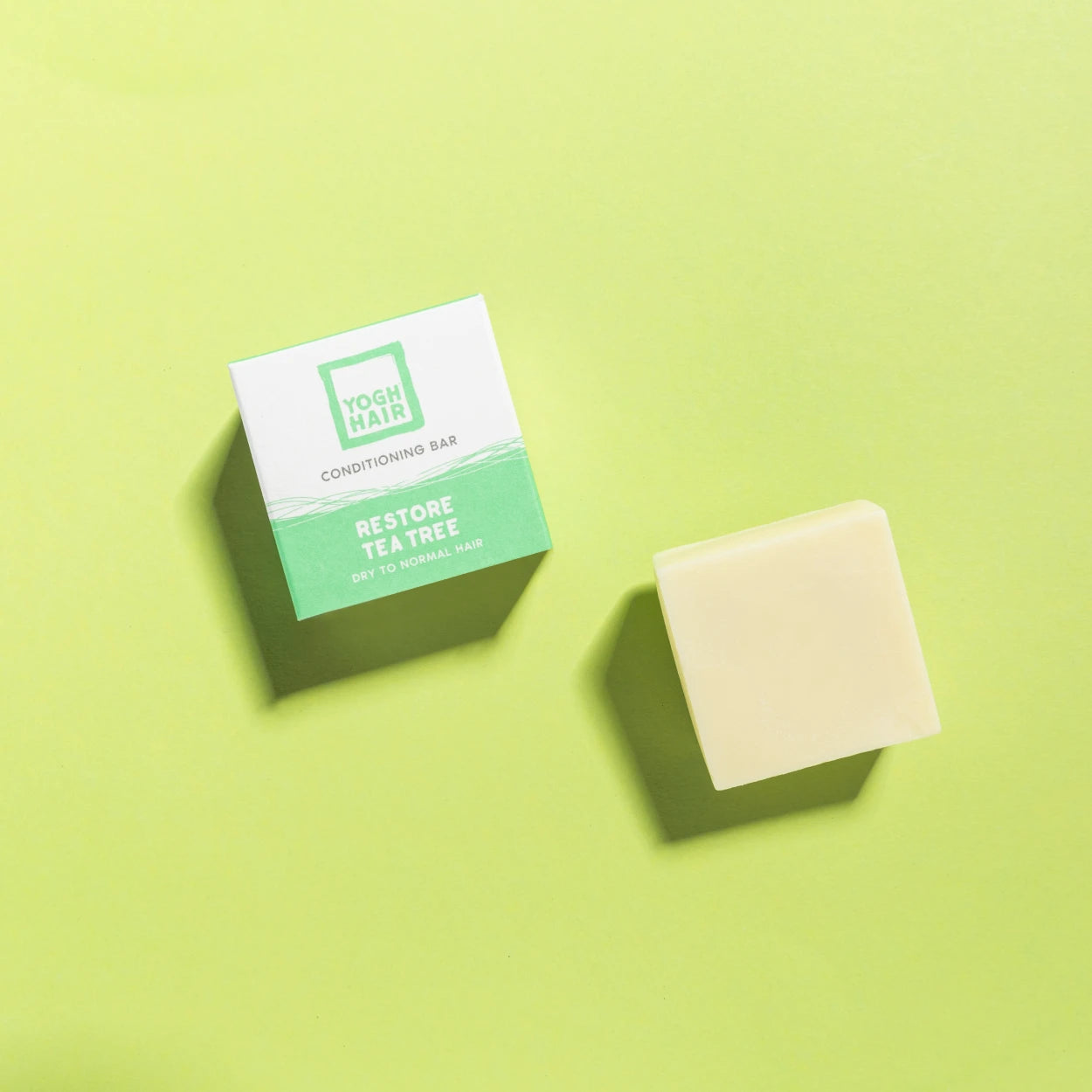 yogh hair restoring conditioner bar with tea tree outside of box on green background