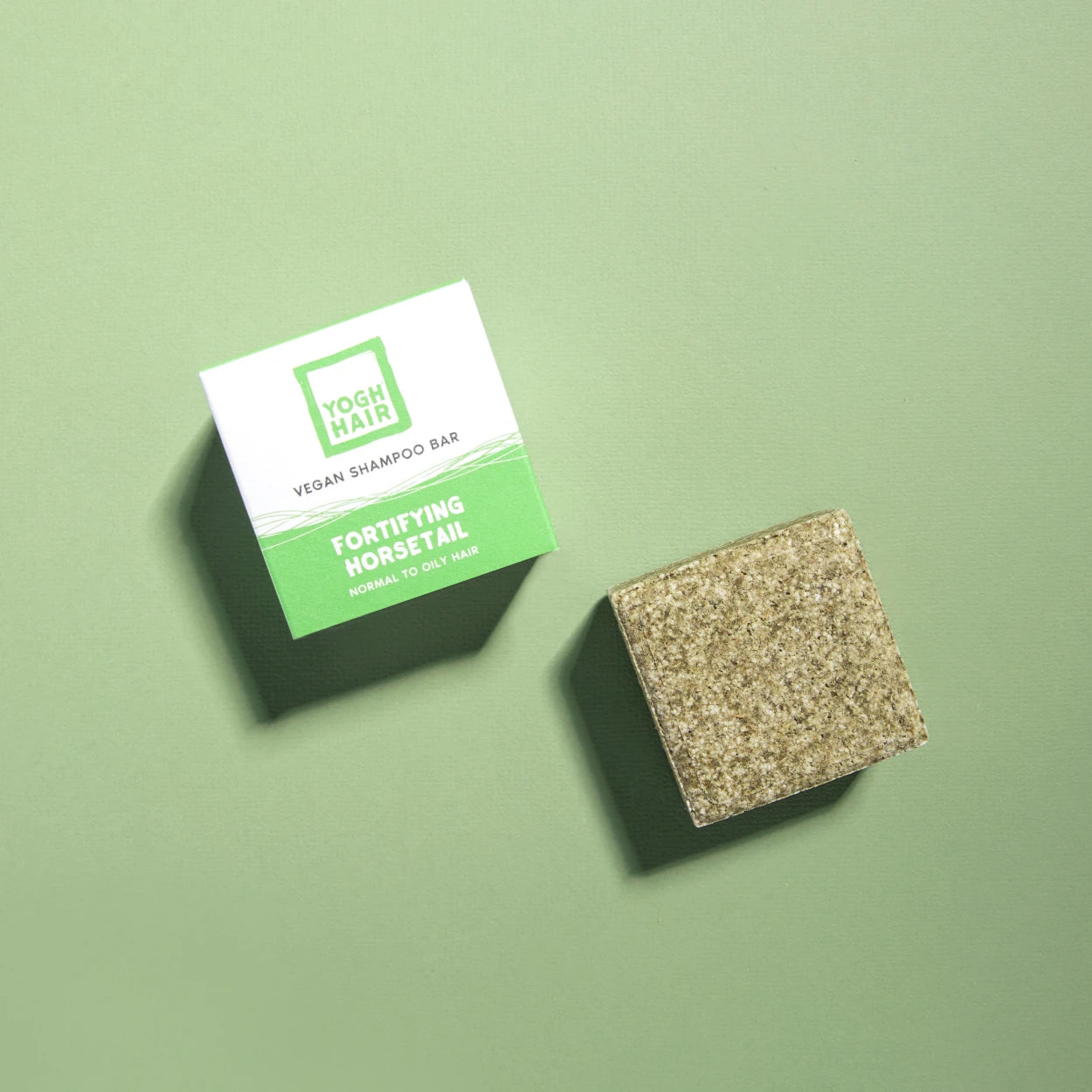 yogh hair fortifying vegan shampoo bar with horsetail and rosemary outside of box on green background