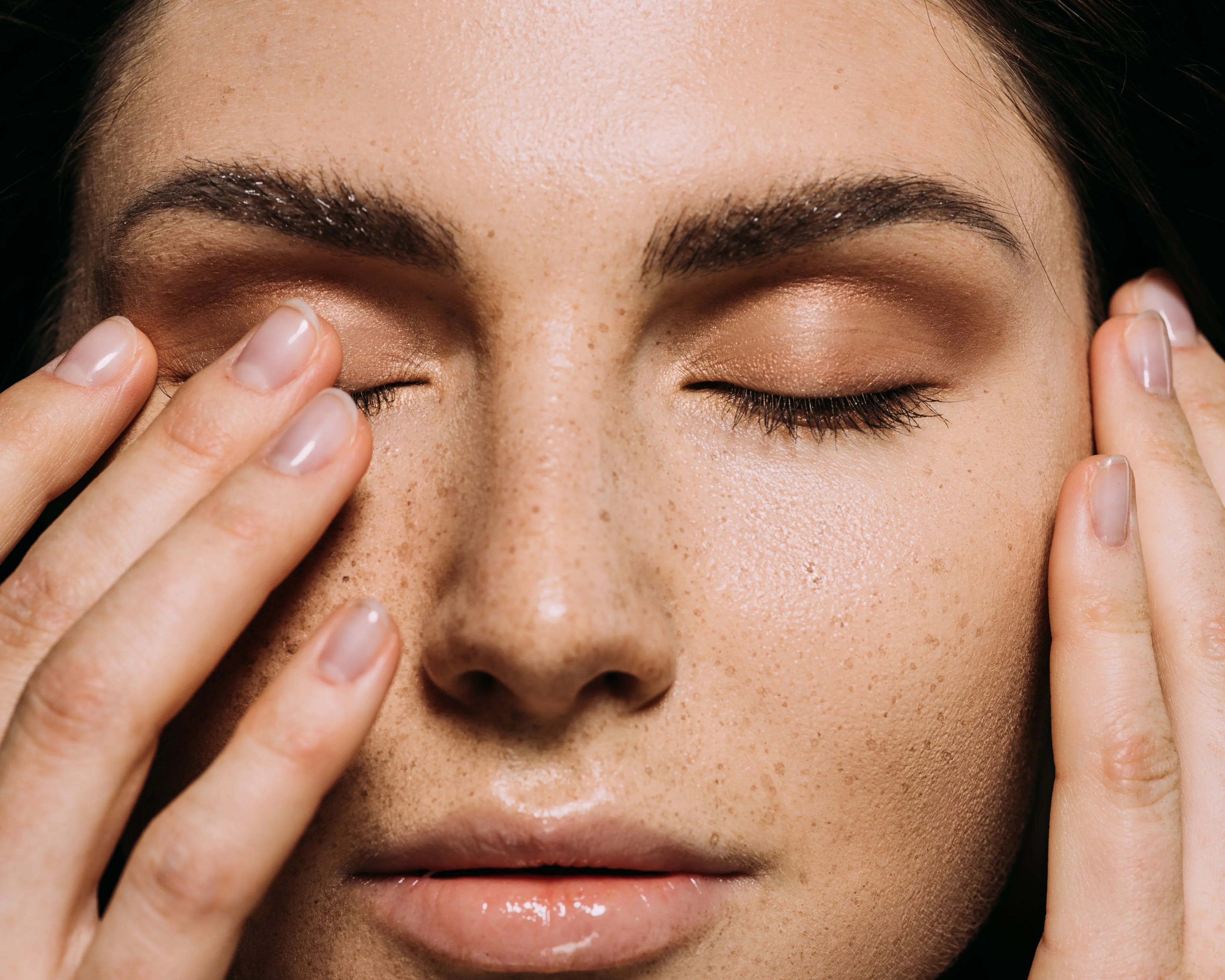 close up view of tender girl with freckles on face touching closed eyes
