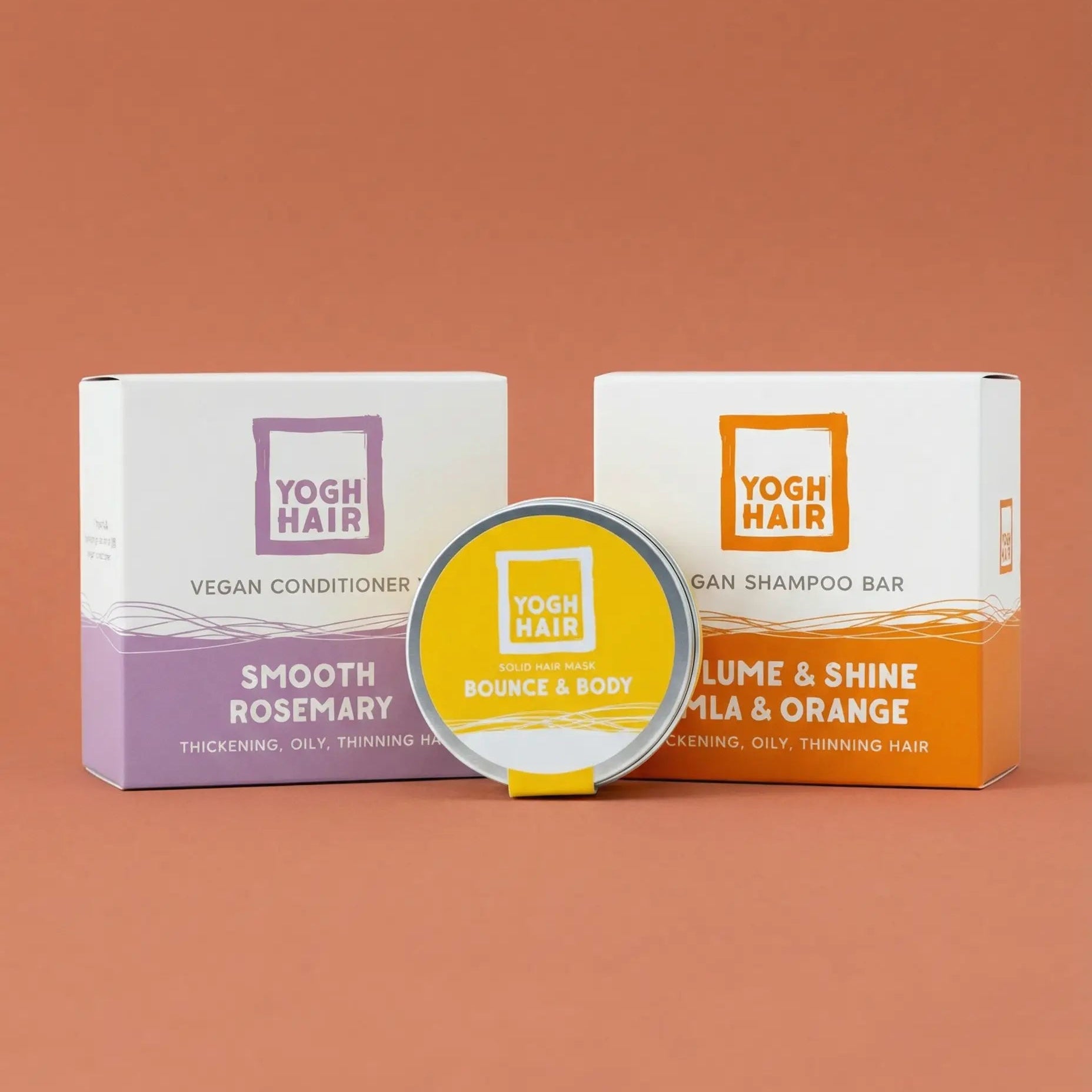 the three products composing the strong hair yoghhair bundle on a soft orange background. the volume shampoo, the thickening conditioner and the hair mask.