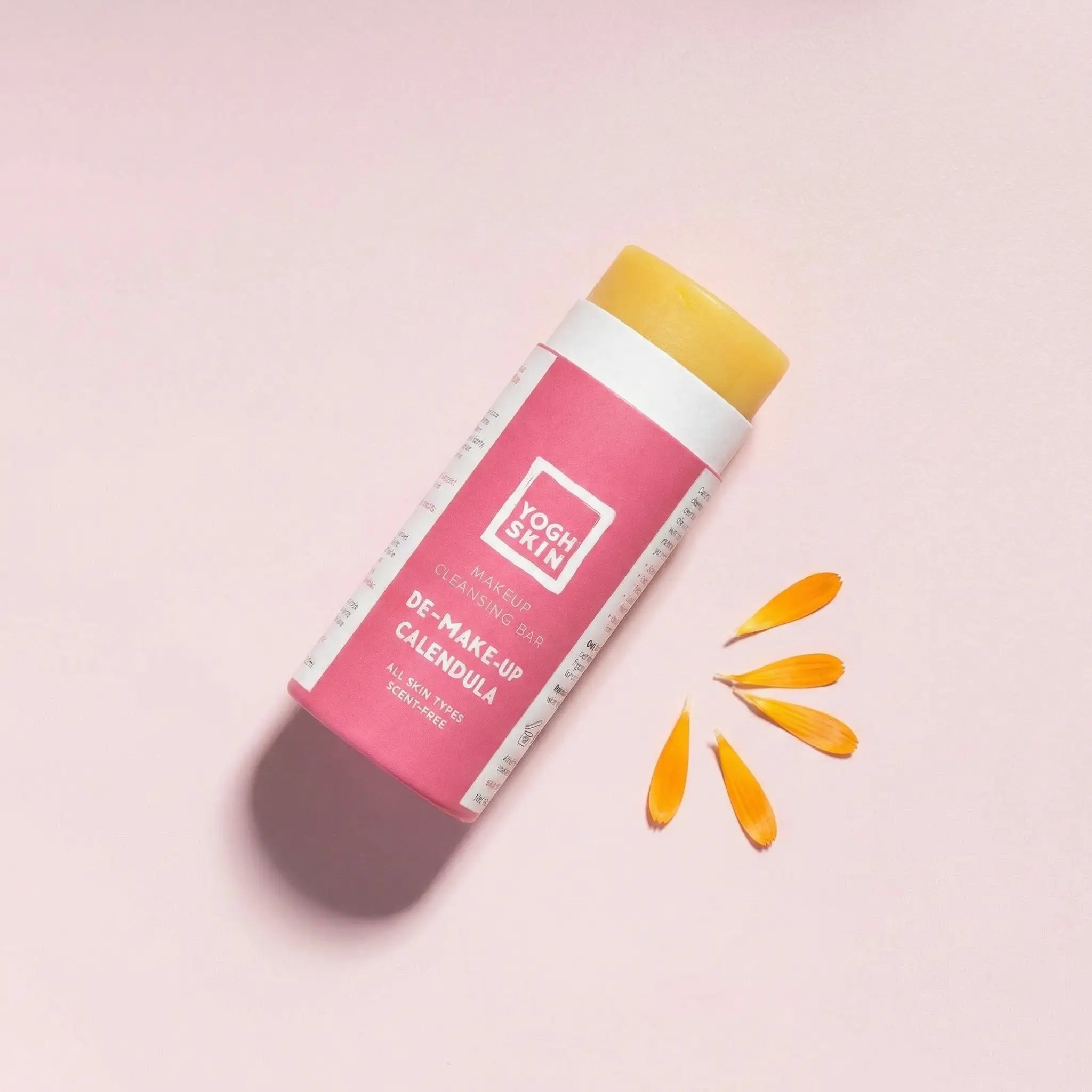 yoghskin solid makeup cleanser without its lid on a pink background next to some calendula petals